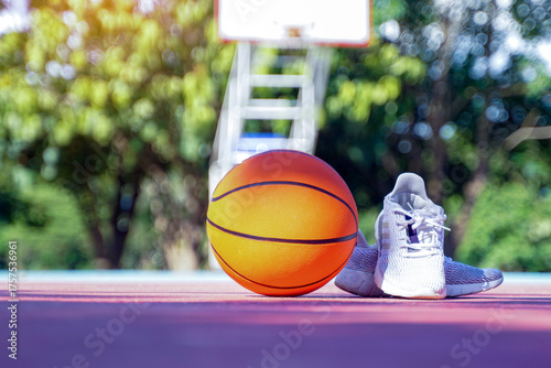 An orange basketball and a pair of white athletic shoes rest on an outdoor court.