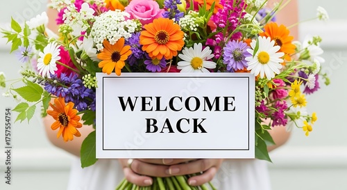 Woman holding a bouquet of colorful flowers with a welcome back sign