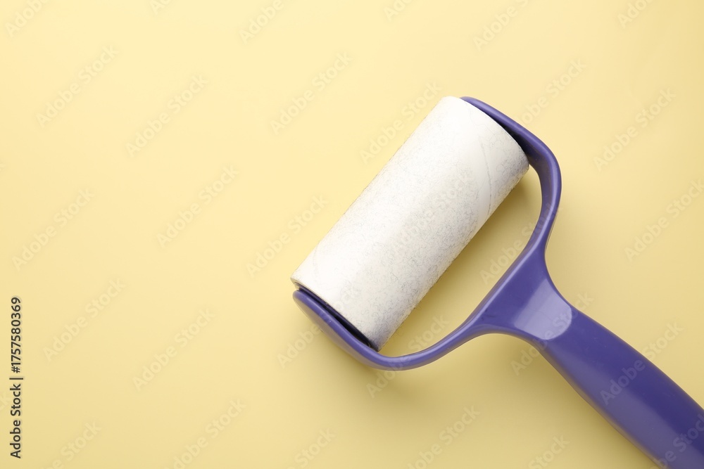 Obraz premium Lint roller with used sticky tape on yellow background, top view. Space for text