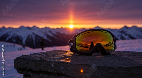 Close-up of ski goggles reflecting a mountain sunset. Winter sports equipment on a rock in a snowy alpine landscape