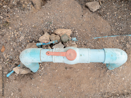 Red Plastic Water Valve on PVC Pipe in Rural Area.