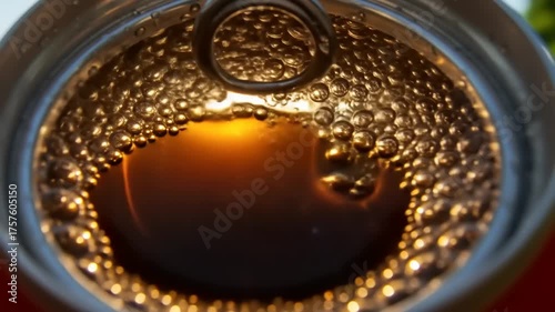 Close-up view of a soda can opening, showcasing bubbles and reflections, surrounded by greenery
