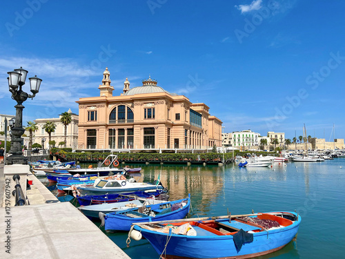 Historisches Theater am Hafen von Bari mit bunten Fischerbooten im Vordergrund, sonniger Himmel und mediterranes Flair an der Adriaküste Apuliens