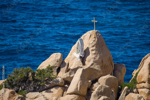 a memorial for sailors on a red rock with the blue sea in the background on the coast of Corsica in the sunshine