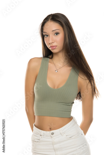 Studio shot of young woman with long brown hair wearing green crop top and white pants, posing confidently, on white background