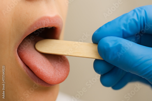 Macro shot of a medical examination where a gloved hand uses a wooden tongue depressor to inspect a patient’s mouth, emphasizing hygiene, precision, and healthcare professionalism.