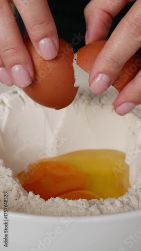 Close-up shot of a woman cracking an egg into flour while making dough for baking.