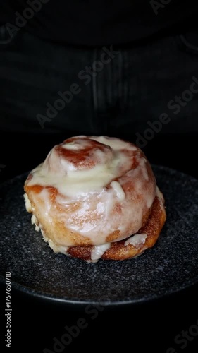 A freshly baked cinnamon roll spins slowly on a plate. Delicious homemade pastry dessert with sweet icing, perfect for breakfast or coffee time. Concept of home baking and confectionery.