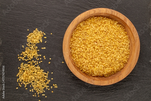 Bulgur in a wooden plate on a slate stone, close-up, top view.