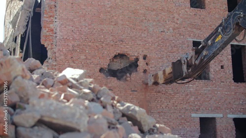 Excavator demolishing brick wall of old building