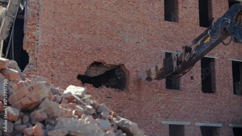 Excavator arm demolishing brick wall of old building