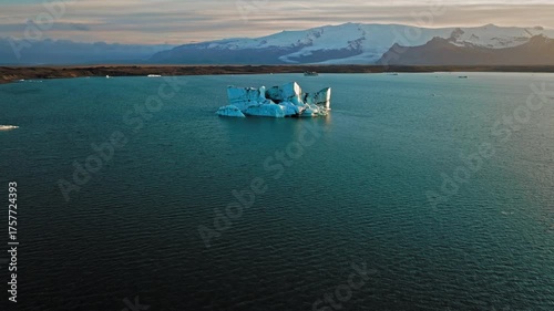 Large iceberg floating at Jokulsarlon glacier lagoon Iceland. Drone captures a massive blue iceberg drifting silently on calm glacial water under soft light.