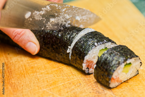 Person Slicing Homemade Sushi Roll With Salmon and Cucumber On Wooden Cutting Board