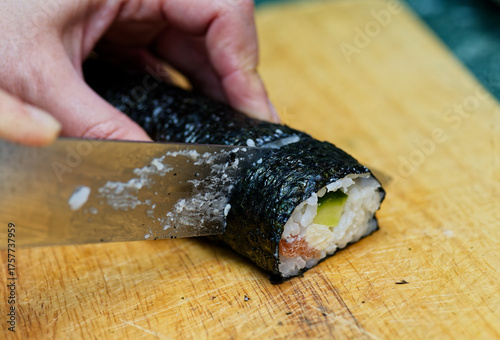 Hand Cutting Sushi Roll On Wooden Board With Fresh Salmon And Cucumber