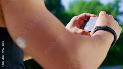 Tight shot of a fit man checking his glucose levels with wearable sensors during an outdoor run in a scenic park.