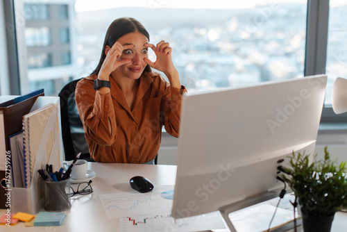 Sleepy businesswoman trying to stay awake keeping her eyes opened with fingers, looking at desktop computer monitor