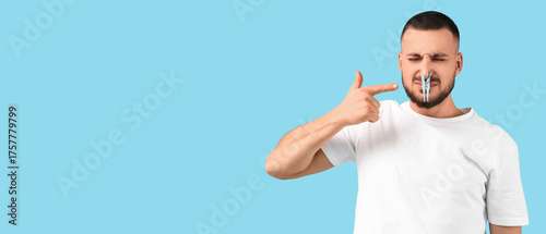Young man pointing at clothespin on blue background. Stuffy nose concept