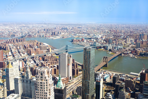High-angle panoramic view of a modern city with tall skyscrapers, bridges, and a wide river under clear blue skies, representing urban development and architecture.
