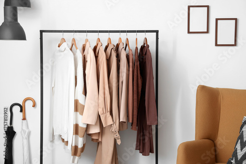 Rack with hanging clothes near white wall in room, closeup