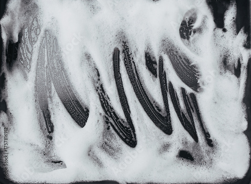 White foam and soap on dark background. The concept of washing oily pan or black car. Abstract pattern.