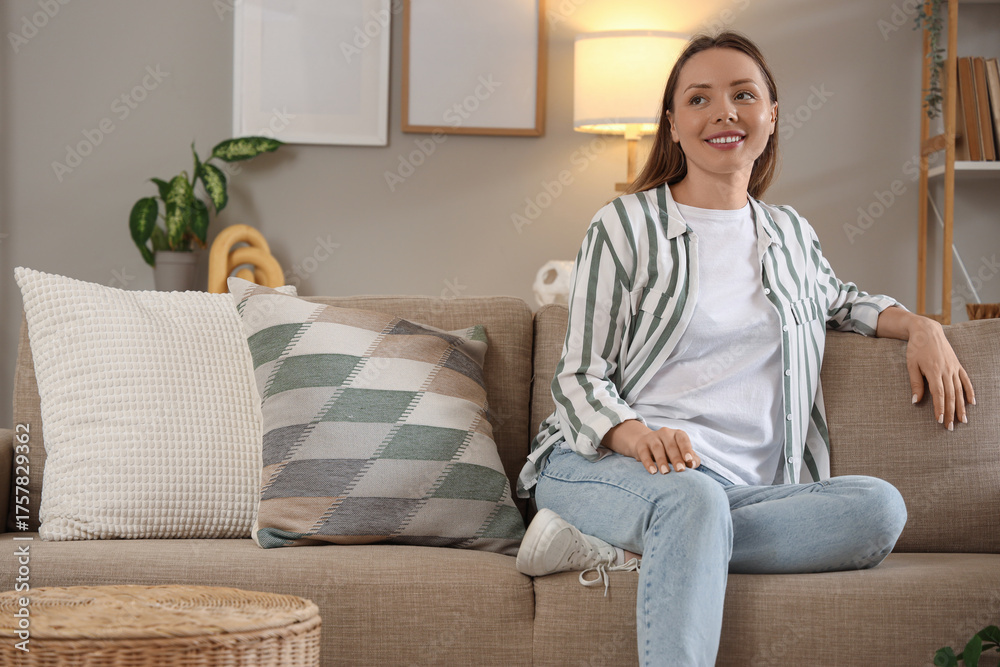 Fototapeta premium Dreamy young woman sitting on sofa at home