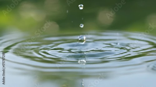 Mesmerizing slow motion close-up of crystal clear water drops gracefully falling and creating intricate ripples in a calm, reflective pond surface meditative, liquid, abstract