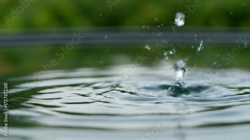 Mesmerizing slow motion close-up of crystal clear water drops gracefully falling and creating intricate ripples in a calm, reflective pond surface meditative, abstract, beautiful