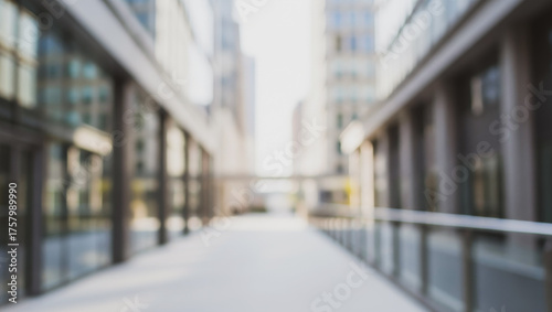 Blurred modern walkway between tall office buildings on a bright day, capturing the soft glow of sunlight reflecting off glass surfaces and creating a serene yet dynamic urban perspective.