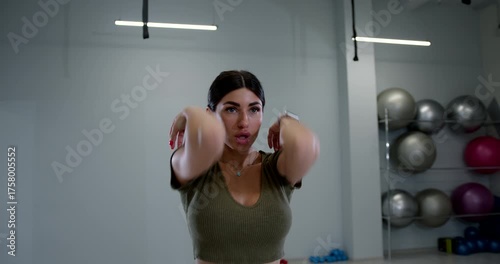 athletic woman is actively engaging in shoulder rotations to improve her flexibility and strength in a modern gym environment. The space features various workout equipment.