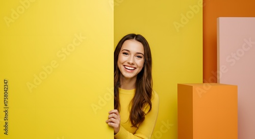 Smiling woman peeking from behind a yellow wall.
