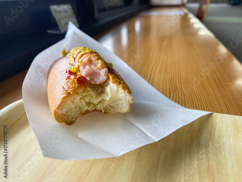 トマトケチャップとマスタードソースをトッピングしたジューシーなホットドッグ。食べている途中。