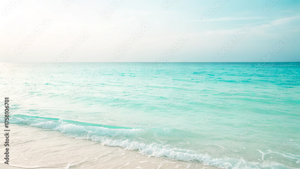 Obraz premium Gentle waves lap against a soft sandy shore as the sun rises over a tranquil beach. The clear turquoise water sparkles under the morning light, creating a peaceful atmosphere