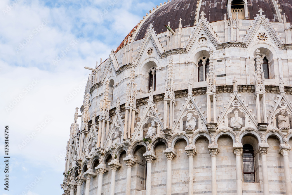 Fototapeta premium Ornate Gothic dome of Pisa Baptistery with white marble arcades, pointed arches, decorative spires and weathered copper cupola against blue sky in Tuscany Italy