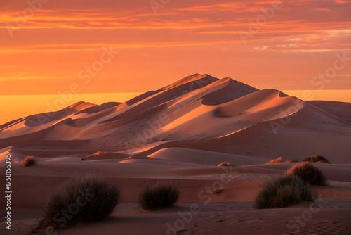 Fototapeta Naklejka Na Ścianę i Meble -  Majestic desert dunes sculpted by wind under a vibrant orange and yellow sunset sky creating dramatic shadows and highlights