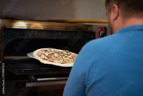 Close-up portrait a cheerful chef working in a pizza place and putting the pizza into the owen. Smiling chef wearing apron uniform and posing. Space for text.