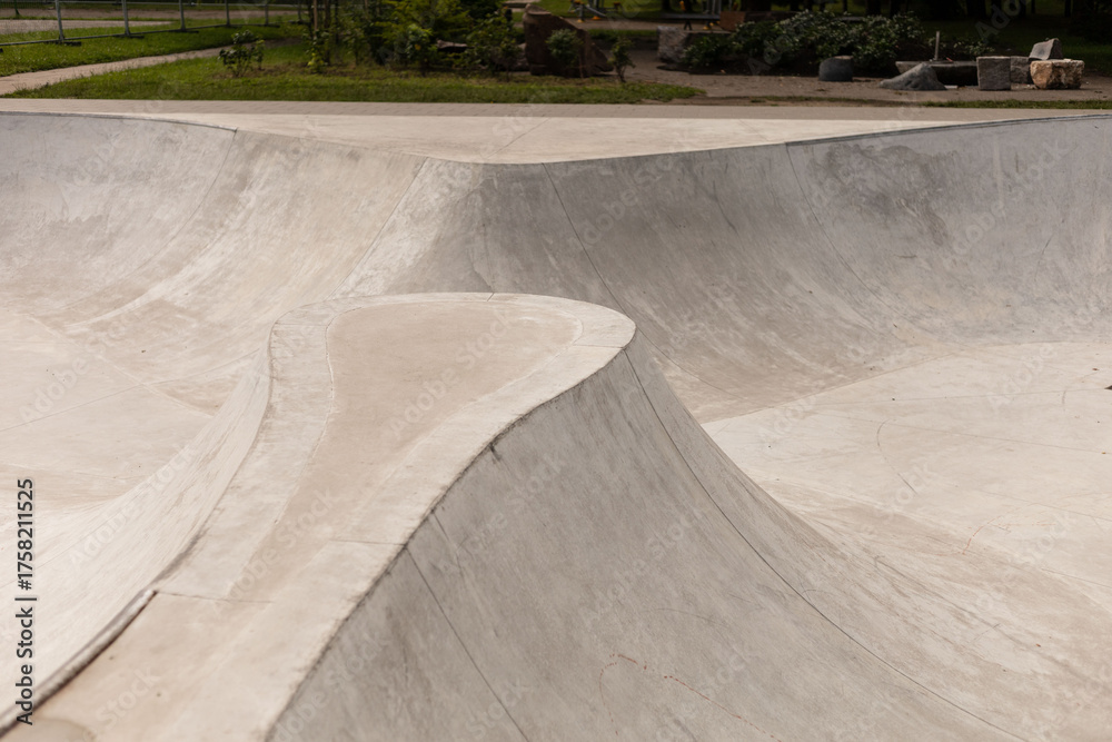 Fototapeta premium A modern skatepark showcases flowing concrete surfaces and ramps designed for skateboarders and BMX riders to practice tricks and skills. The location features greenery nearby