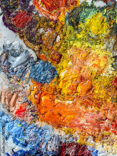 Vibrant textured oil paint palette in warm and cool colors. Creative mess of artist tools.