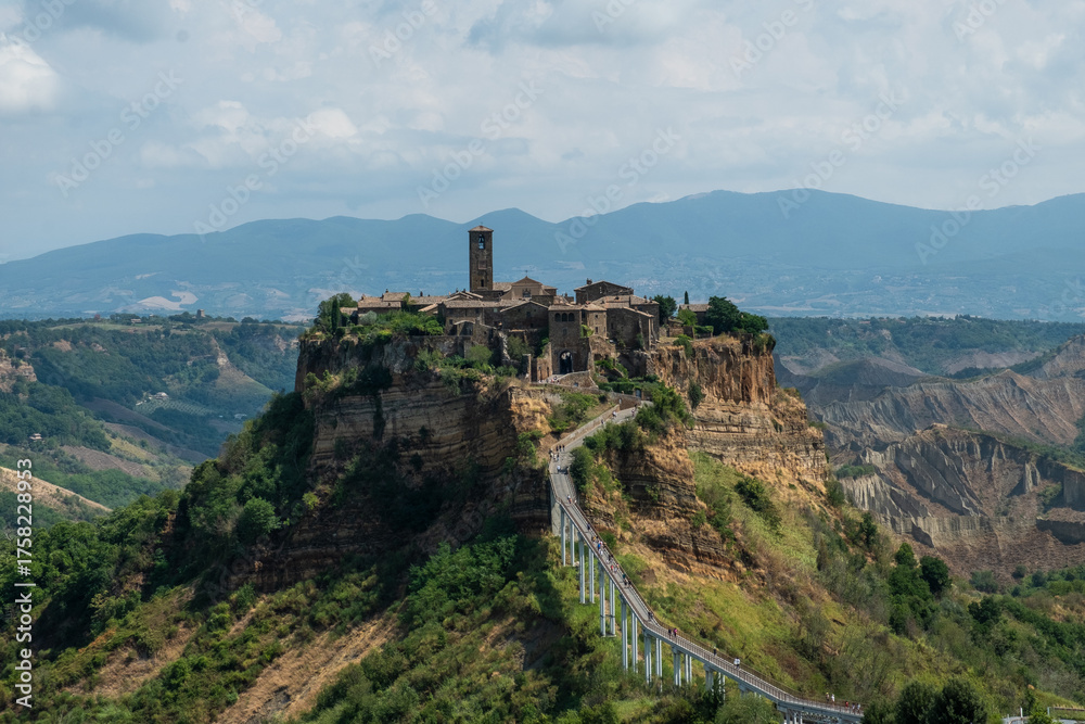 Fototapeta premium Civita di Bagnoregio, in central Italy, features medieval stone buildings, a prominent bell tower, and breathtaking views of surrounding valleys and mountains.