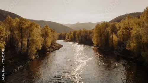 River flows between autumnal trees and rolling hills, under soft daylight