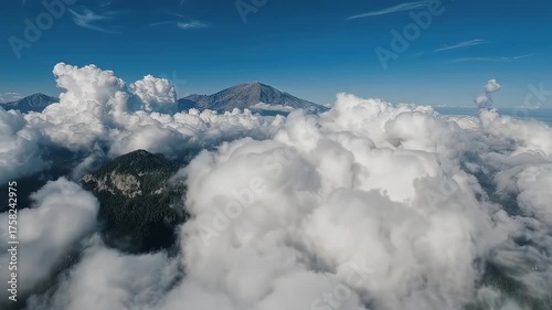 Aerial view of mountain peaks surrounded by clouds under a blue sky