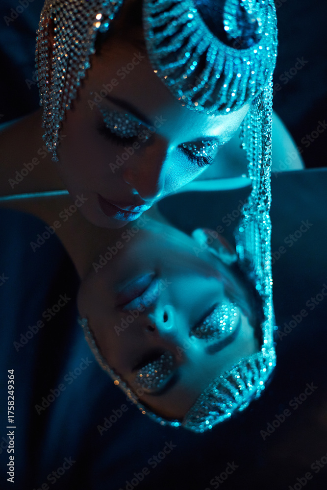© angel_nt - woman in a stunning headpiece with glittering makeup looks down at her reflection in a mirror. blue lighting enhances the artistic atmosphere of an evening art event © angel_nt - woman in a stunning headpiece with glittering makeup looks down at her reflection in a mirror. blue lighting enhances the artistic atmosphere of an evening art event