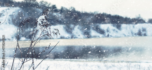 Quadro su tela Snowfall on a frosty winter day over snow-covered hills and a frozen river or la