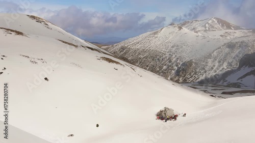 Group of mountaineers resting by a rock in a snowy alpine valley under a bright sky.