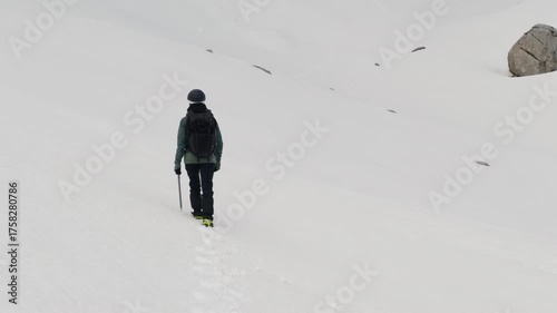 Solo hiker walking through deep snow with backpack and ice axe in a white alpine landscape.