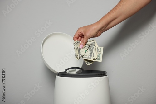 Fotografie Woman throwing dollar banknotes into trash bin near light wall indoors, closeup