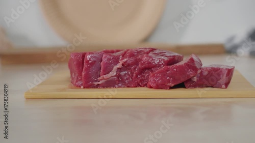 A piece of fresh beef is placed on a wooden cutting board in a bright kitchen.