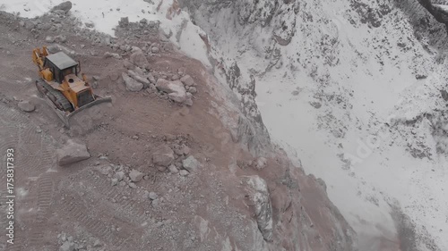 A tractor throws rocks off a cliff.