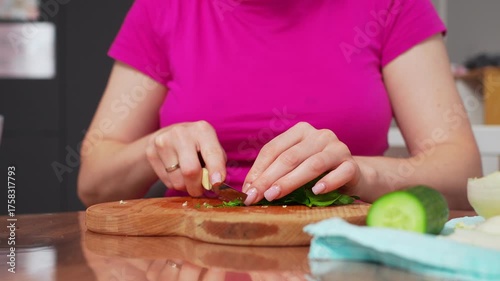 Hands skillfully chop fresh herbs on a wooden board.