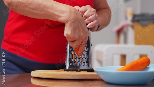 A person is grating fresh carrots in a well-lit kitchen. The kitchen is warm and inviting