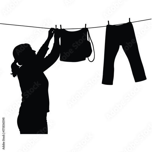 Silhouette of a woman hanging clothes on a clothesline with a shirt and pants outside to dry